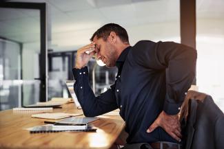 man rubbing his back painfully at his desk